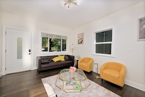 A living room with a dark brown leather sofa, a yellow armchair, a glass coffee table, and a white door.