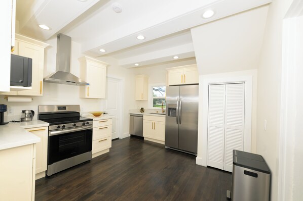 A modern kitchen with stainless steel appliances, white cabinetry, and a dark wood floor.