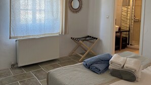 Ein Schlafzimmer mit Bett, Heizkörper, einem Fenster mit Vorhängen, einem Handtuchhalter und einer Tür zu einem Badezimmer.