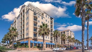 A multi-story hotel with balconies, palm trees, and a clear sky.