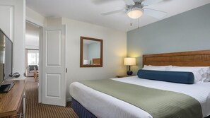 A hotel room with a bed, bedside table, lamp, ceiling fan, and a view of the hallway.