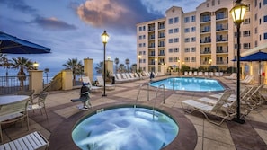 A hotel pool area with lounge chairs, a hot tub, and a building with multiple balconies.