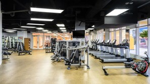 Un gimnasio con cintas de correr, máquinas de pesas y un espejo grande.