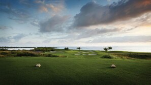Campo de golf con búnkeres, un cuerpo de agua y vista al océano.