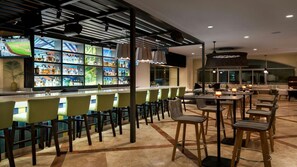 Zona de bar con mostrador, taburetes y un área de estar con mesas y sillas.
