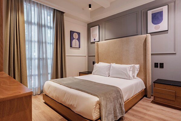 A hotel room with a large bed, wooden headboard, a nightstand, a wooden dresser, and a window with curtains. - Stylish Roma Norte Loft + Concierge (Ciudad de mexico)