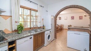 A kitchen with granite countertops, a washing machine, a refrigerator, and a dining area with a brick archway. - El Almendro Cómpeta by Ruralidays (Málaga)