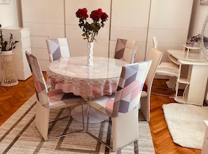 Ein runder Esstisch mit weißer Spitzenleinentischdecke, umgeben von Stühlen mit geometrischen Mustern, und eine Vase mit roten Rosen.