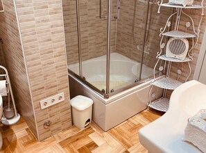 Eine Duschkabine mit Glastür, eine weiße Toilette und ein kleiner weißer Hocker.