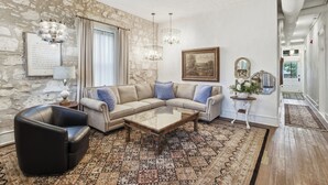 Una sala de estar con una pared de piedra, un sillón de cuero, un sofá modular, una mesa de centro de vidrio y una alfombra estampada.