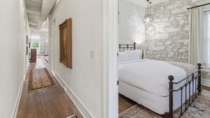 Un dormitorio con cama, pared de piedra y un pasillo que conduce a otra habitación.