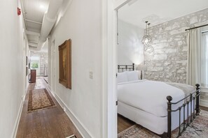 A bedroom with a bed, stone wall, and a hallway leading to another room. - Shopkeeper's Inn (Fredericksburg)