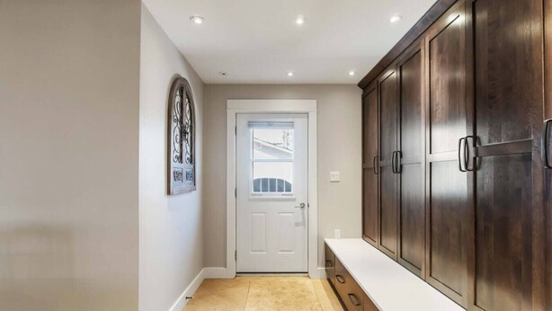 A hallway with a white door, a beige rug, and wooden cabinets.