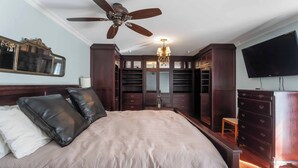 A bedroom with a large bed, a ceiling fan, a chandelier, a TV, and a walk-in closet.