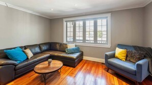 A living room with a sectional sofa, a blue armchair, a round coffee table, and a large window with blinds.