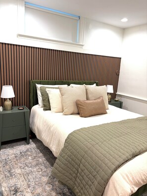 Ein ordentlich eingerichtetes Schlafzimmer mit einem Bett, zwei Nachttischen, einer Lampe und einem Fenster mit Jalousien.