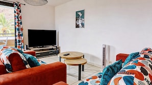 Ein Wohnzimmer mit einer Couch, einem Fernseher, einem kleinen Tisch und einer Deckenleuchte.