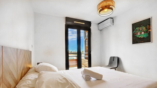 Ein Schlafzimmer mit Bett, Sessel, Fenster und einer Wand-Klimaanlage.