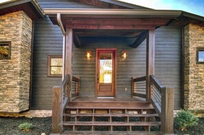 A house with a stone facade, wooden porch, and a front door with a small window above it.