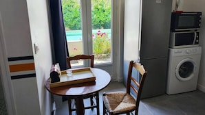 Eine Küche mit Kühlschrank, Mikrowelle und Waschmaschine, einem Esstisch mit Stühlen sowie einem Fenster mit Blick auf Grünflächen und einen Pool.