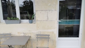 Eine Terrasse mit Tisch und Stühlen, ein Fenster mit Pflanzen und eine Tür.