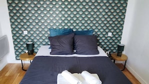 Ein ordentlich bezogenes Bett mit dunkler Bettwäsche, zwei Kissen und zwei gefaltete Handtücher.