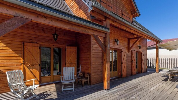 En stuga av trä med en inglasad veranda, två Adirondack-stolar och ett trästaket i bakgrunden.
