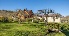 A wooden house with a sloped roof, surrounded by a well-maintained lawn and a small bridge over a stream. - Chalet du moulin - GELLES (GELLES)
