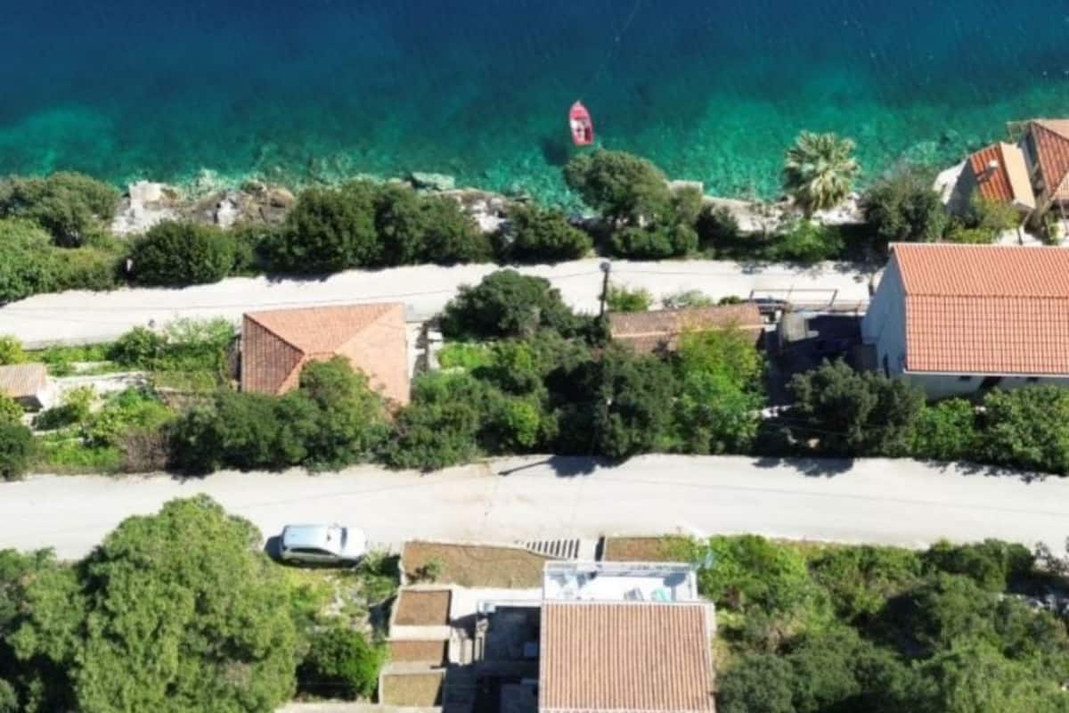 An aerial view of a coastal area with buildings, clear turquoise waters, and a red buoy.