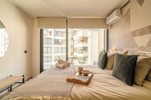 Ein Schlafzimmer mit einem Bett, einem kleinen Tisch mit Tablett, einem Fenster und einer Klimaanlage.