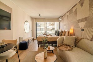Ein modernes Hotelzimmer mit Bett, Sofa, Esstisch und großem Fenster.