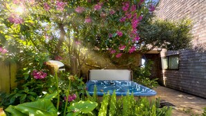 A hot tub surrounded by lush greenery and flowering plants in a backyard setting.