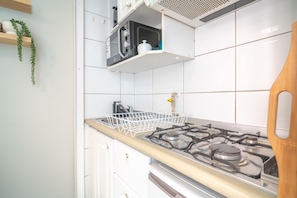 Une cuisine équipée d’une cuisinière à gaz, de meubles blancs, d’un four à micro-ondes et d’une plante suspendue.