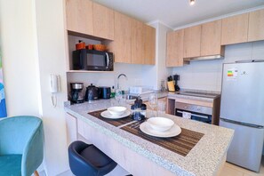 A modern kitchen with granite countertops, wooden cabinets, a microwave, a coffee maker, and a refrigerator. - HOM I Wifi Parque Almagro Estreno Calefactor (Santiago)