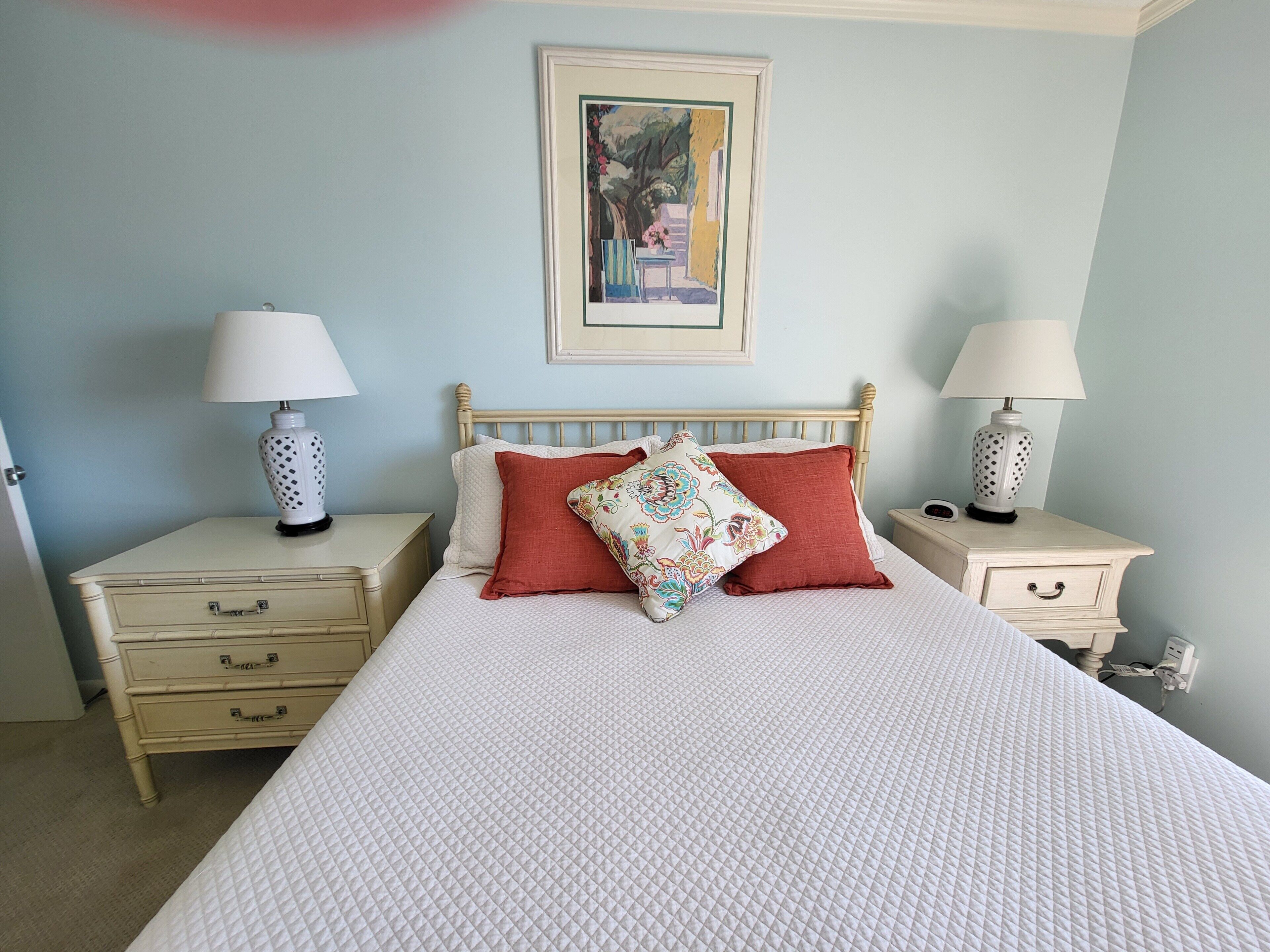 A bedroom with a bed, two bedside tables, a nightstand, a lamp, a framed picture on the wall, and a dresser.