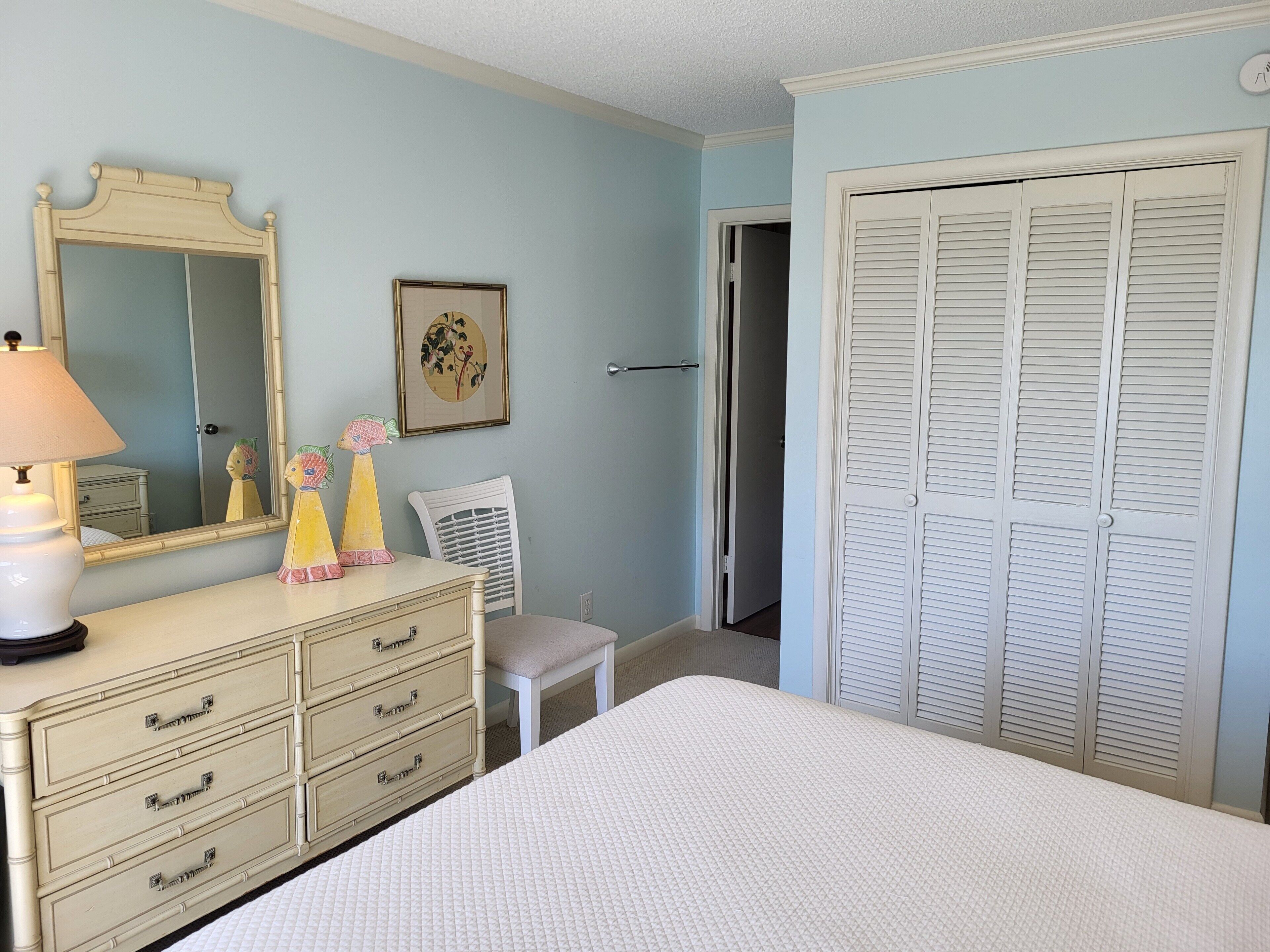 Quarto com cama, penteadeira, espelho e uma porta com venezianas.