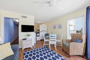 A living room with a TV, a dining table, a sofa, a patterned rug, and a wicker chair. - A Place At The Beach 213 - Coastal Calm Meets Resort Fun! (Atlantic Beach)