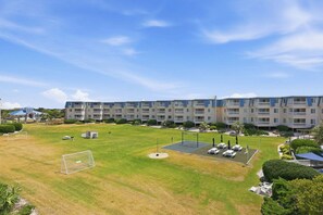 A hotel with multiple balconies, a grassy courtyard with a soccer goal, and a pool area. - A Place At The Beach 213 - Coastal Calm Meets Resort Fun! (Atlantic Beach)