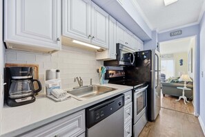 A modern kitchen with white cabinets, a built-in microwave, a coffee maker, and a dishwasher. - A Place At The Beach 213 - Coastal Calm Meets Resort Fun! (Atlantic Beach)