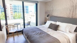 A modern hotel room with a large bed, a small balcony, and a view of the cityscape. - HOM TOP1 | Las Condes | Parque Arauco | Parking (Las Condes)