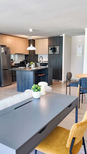 A modern kitchen with a central island, stainless steel appliances, and a dining area with a table and chairs. - HOM TOP1 | Las Condes | Parque Arauco | Parking (Las Condes)