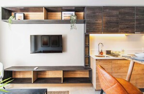 Une cuisine moderne dotée de meubles de rangement en bois intégrés, d’un téléviseur fixé au mur et d’un espace détente avec des bancs.