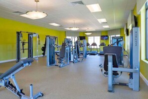 A gym with various exercise machines, a television on the wall, and a bright yellow wall. - Themed Kids Bedrooms | Theater Area | No Rear Neighbors (Kissimmee)