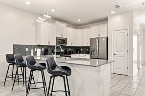 A modern kitchen with white cabinets, stainless steel appliances, and a central island with bar stools. - Themed Kids Bedrooms | Theater Area | No Rear Neighbors (Kissimmee)