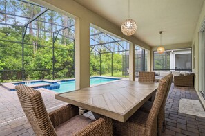 A covered outdoor area with a pool, wicker furniture, and large windows offering a view of the surrounding greenery. - Themed Kids Bedrooms | Theater Area | No Rear Neighbors (Kissimmee)