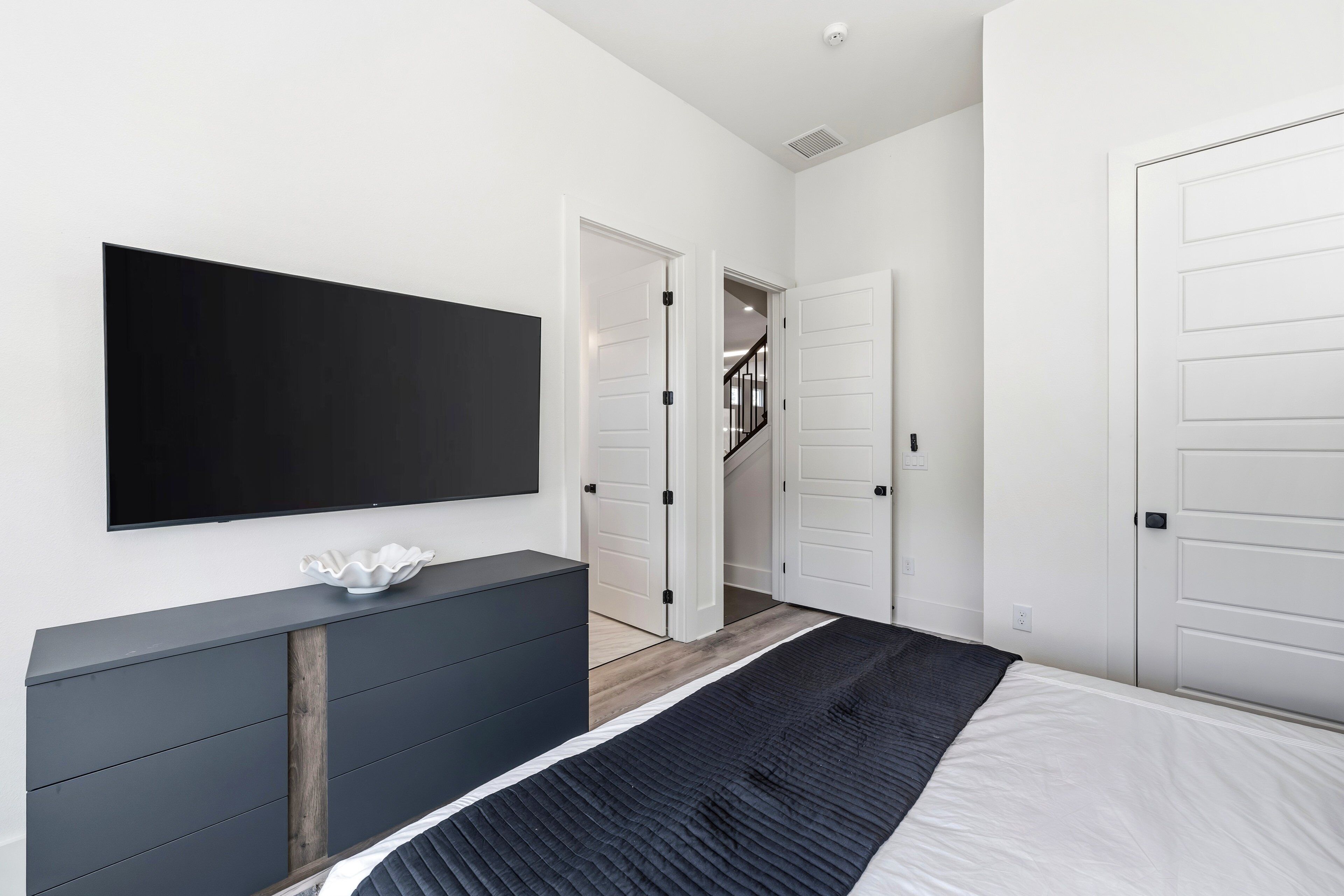 A modern bedroom with a bed, a TV, a dresser, and a staircase leading to another room.