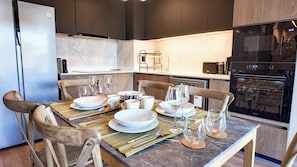A modern kitchen with a dining table set for four, equipped with a refrigerator, oven, microwave, and a coffee machine. - HOM | Aire Acondicionado I Providencia | Parking (Providencia)