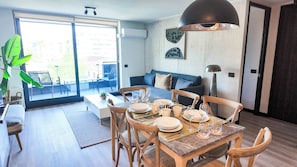 A modern living space with a dining area, a sofa, and a large window. - HOM | Aire Acondicionado I Providencia | Parking (Providencia)