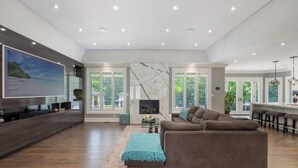 A spacious living room with a large flat-screen TV, a comfortable sofa, and a kitchen area with bar stools. - Luxury Private Estate Retreat. 
Pool • Hot Tub • Gym • Pool Table (Halton Hills)