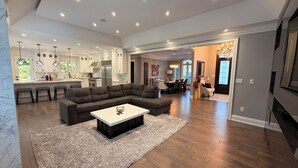 A modern living room with a sectional sofa, a coffee table, and a kitchen in the background. - Luxury Private Estate Retreat. 
Pool • Hot Tub • Gym • Pool Table (Halton Hills)